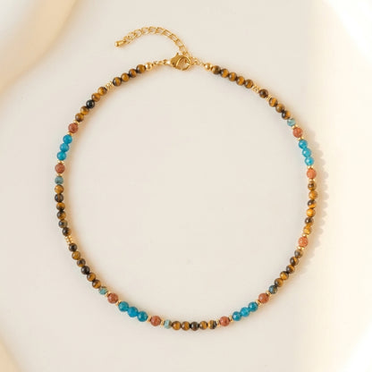 Artisanal gemstone choker featuring natural tiger's eye, blue apatite, and sandstone held delicately by hand.