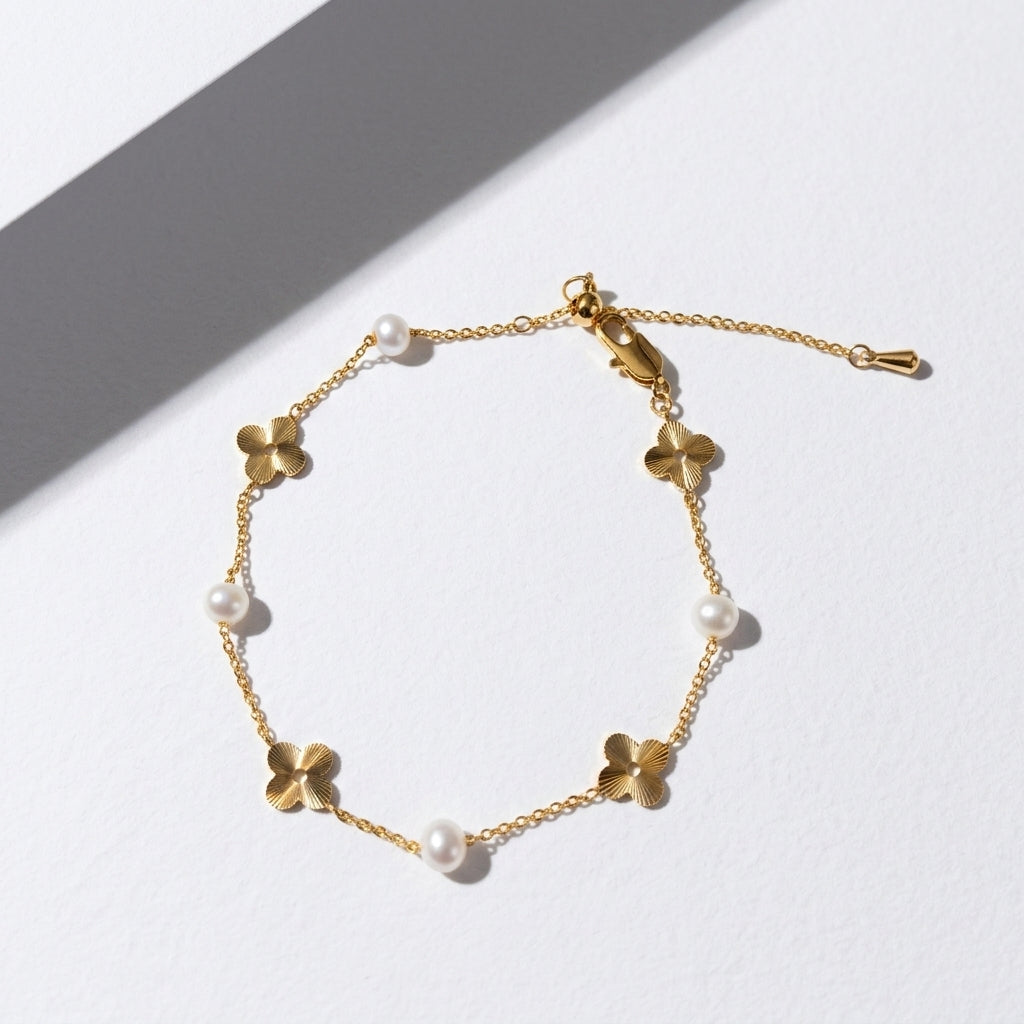 Minimalist 14K gold and pearl floral bracelet styled on a white geometric plaster prop.