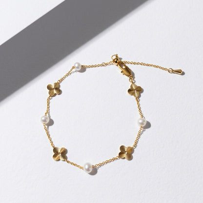 Minimalist 14K gold and pearl floral bracelet styled on a white geometric plaster prop.