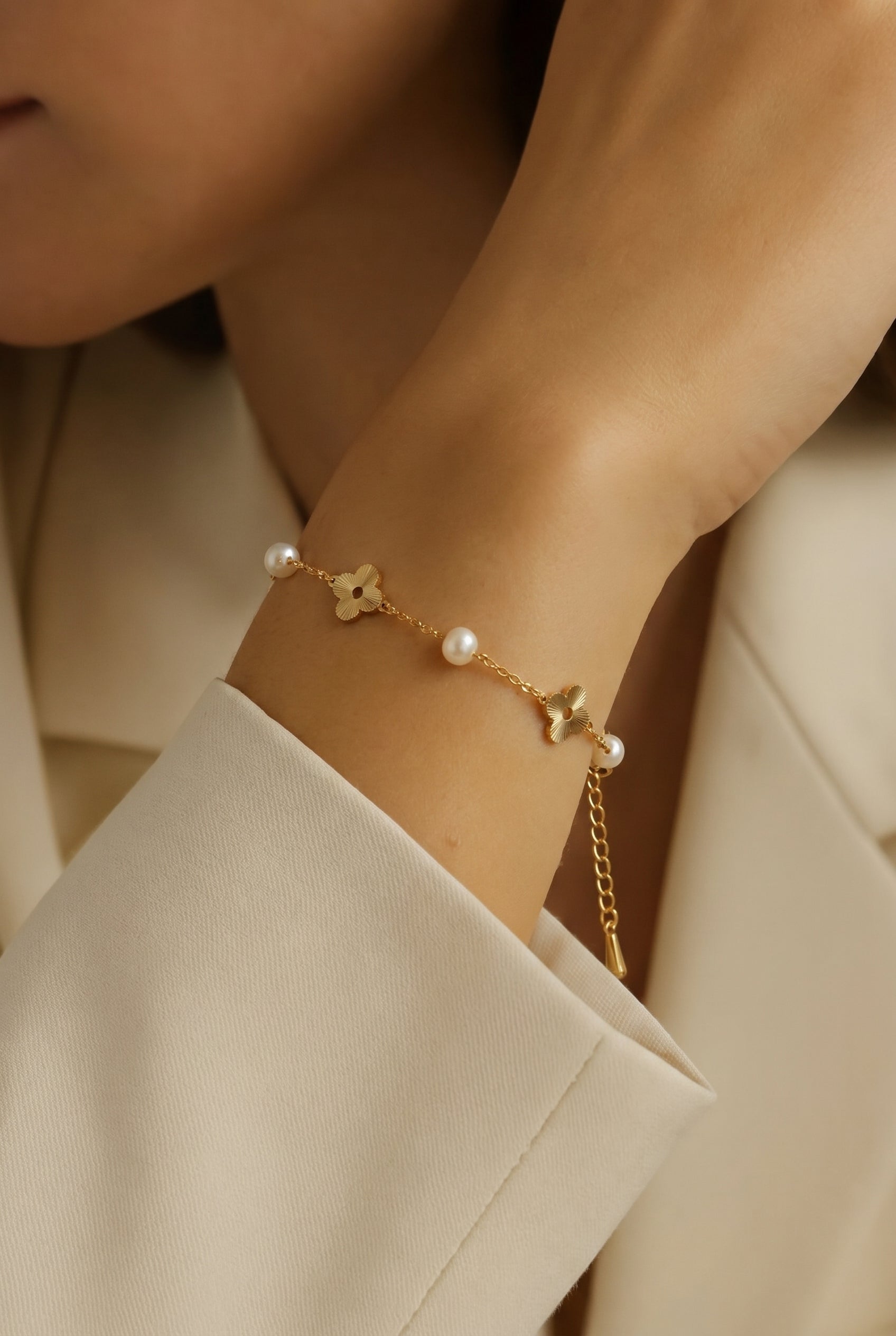 Model wearing the dainty Flora Whisper pearl and gold floral bracelet, hand gently resting near her collarbone.