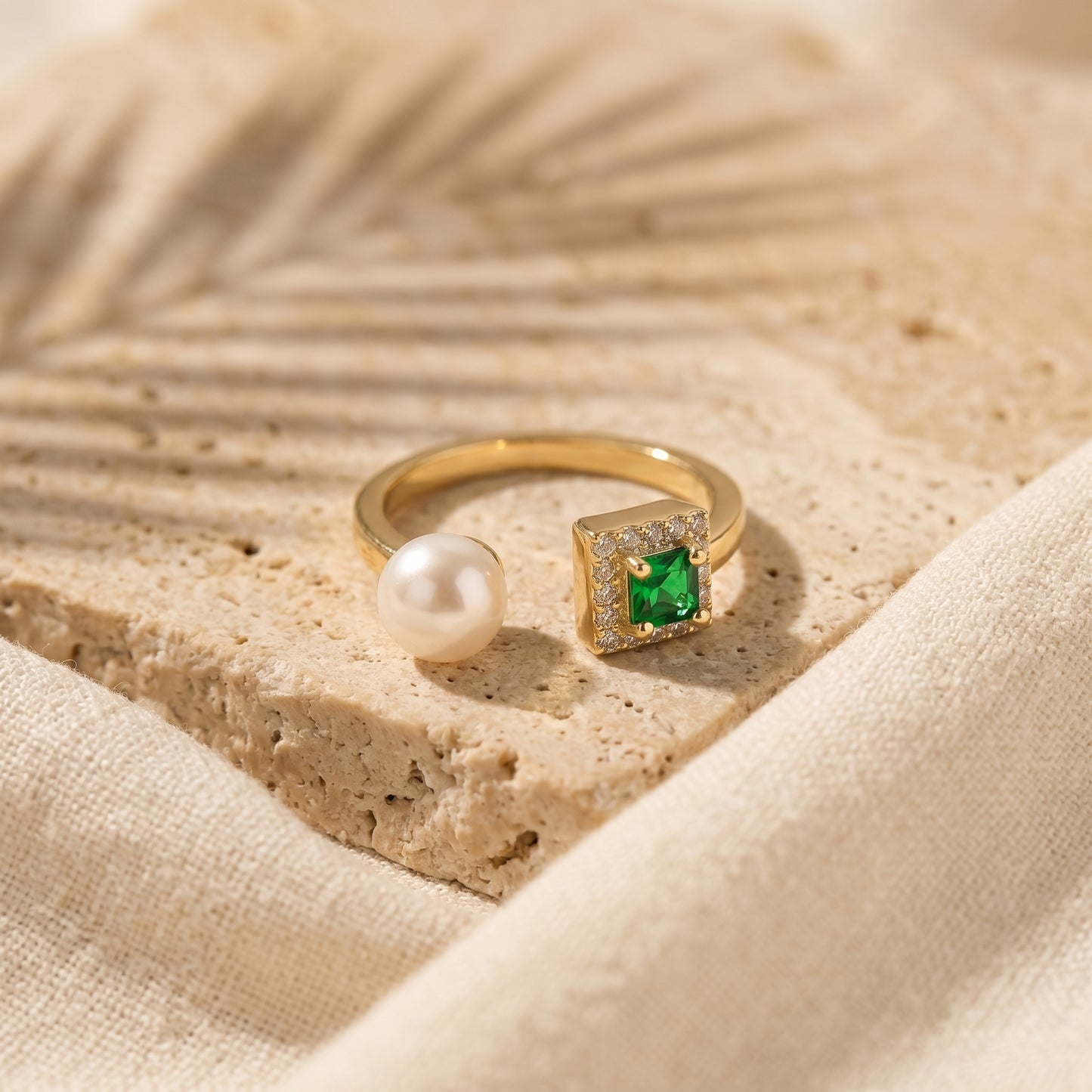 The 'Muse' gold-plated emerald ring displayed on a natural textured stone surface.