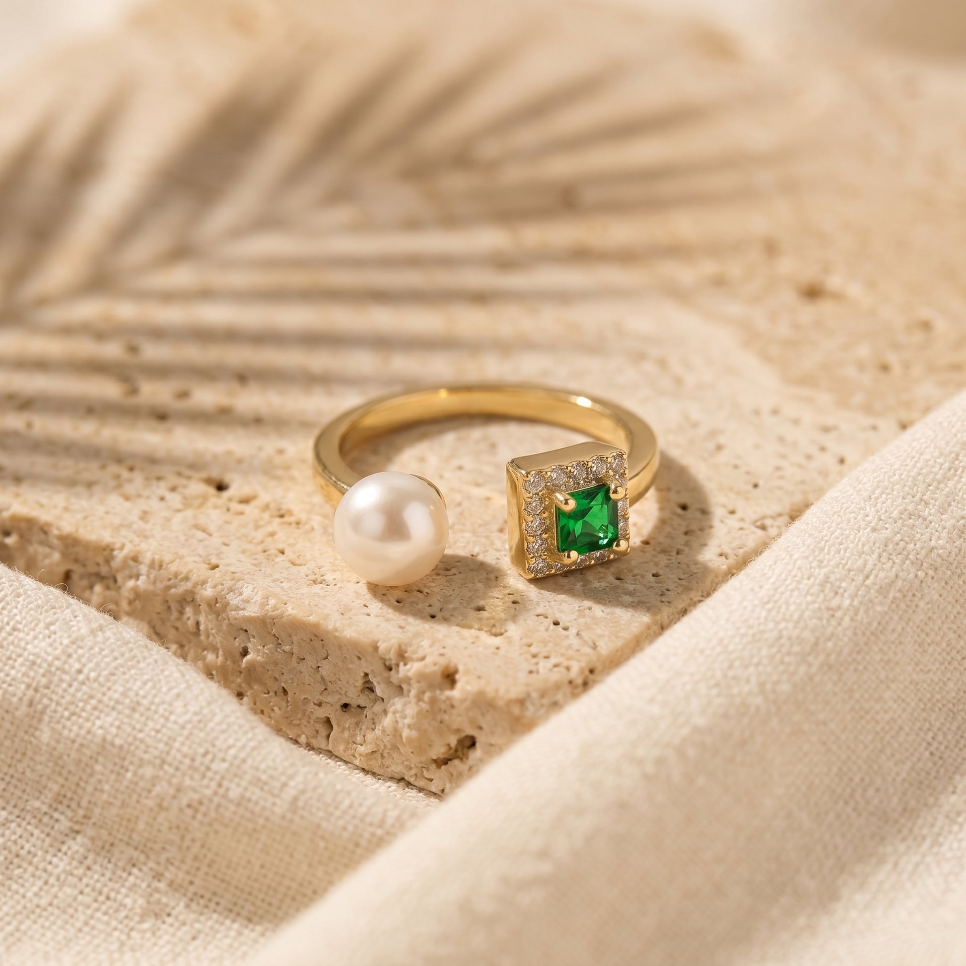 The 'Muse' gold-plated emerald ring displayed on a natural textured stone surface.