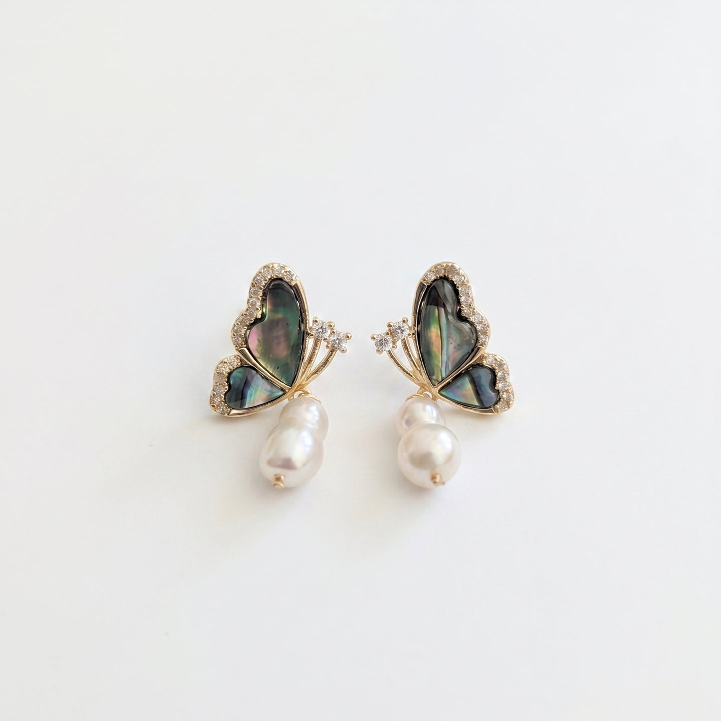A pair of minimalist dangle earrings featuring natural baroque freshwater pearls and abalone butterfly tops.