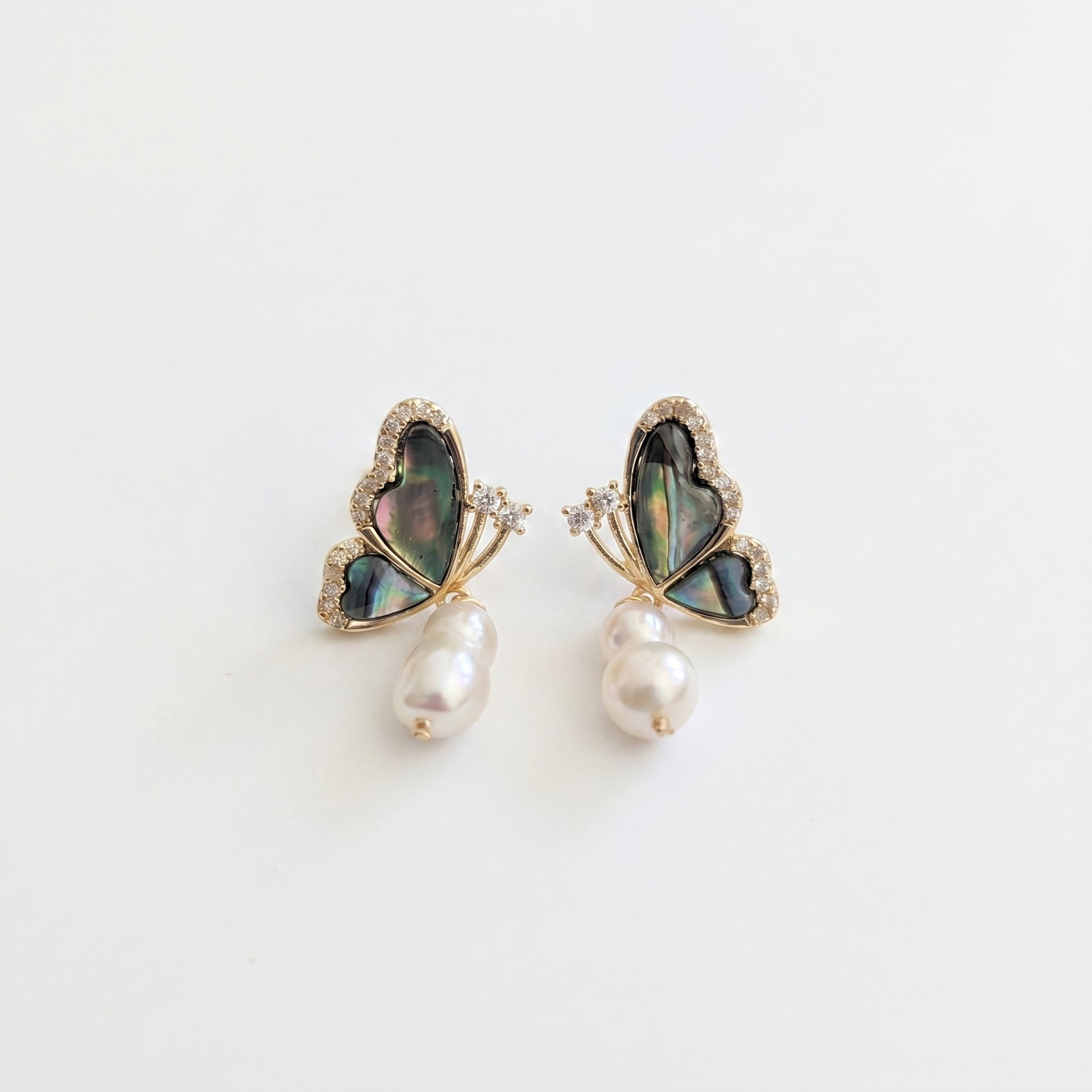 A pair of minimalist dangle earrings featuring natural baroque freshwater pearls and abalone butterfly tops.