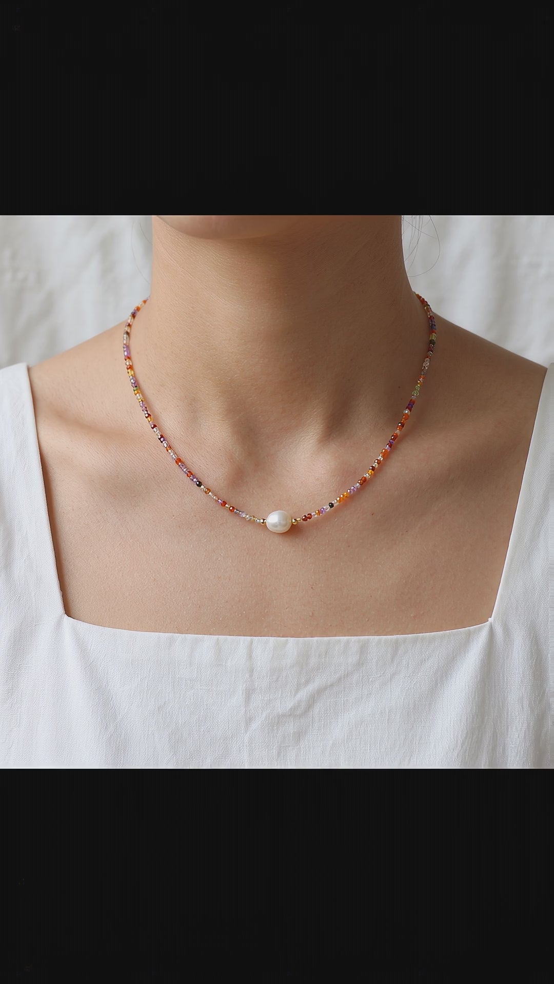 Video showcase of a model wearing the Sunrise Whisper dainty colorful beaded necklace with a central freshwater pearl, styled with a white square-neck top by Whisperland Studio.