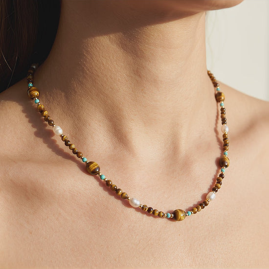 Video of model wearing Tierra choker with natural tiger's eye, turquoise, and natural baroque pearls in warm light.