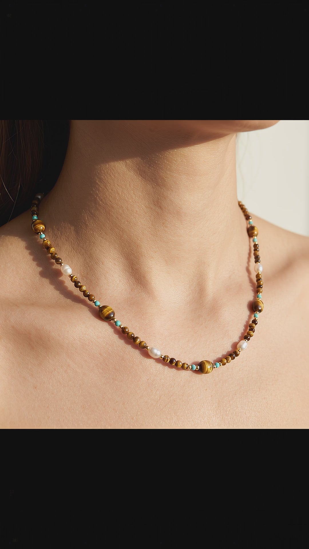 Video of model wearing Tierra choker with natural tiger's eye, turquoise, and natural baroque pearls in warm light.