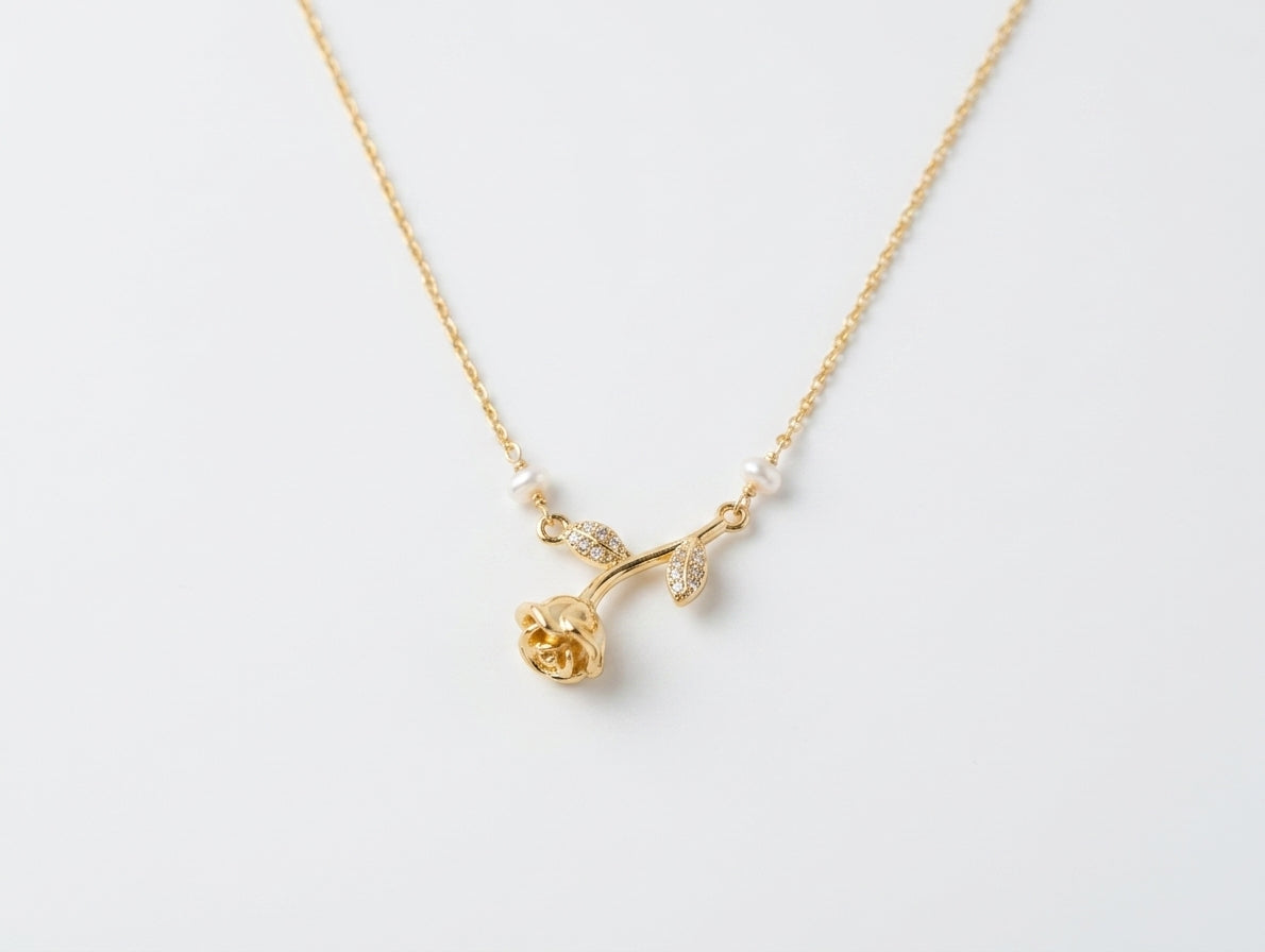 A delicate gold necklace featuring a rose-shaped pendant with small white pearl accents and tiny clear stones, displayed on a clean white background.