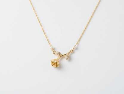 A delicate gold necklace featuring a rose-shaped pendant with small white pearl accents and tiny clear stones, displayed on a clean white background.