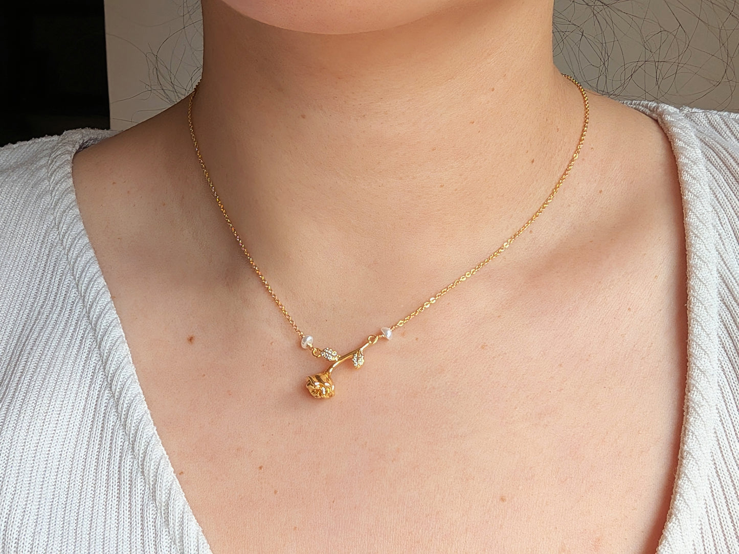A close-up of a person's neck and chest wearing a delicate gold necklace with a small floral pendant and tiny clear stones.