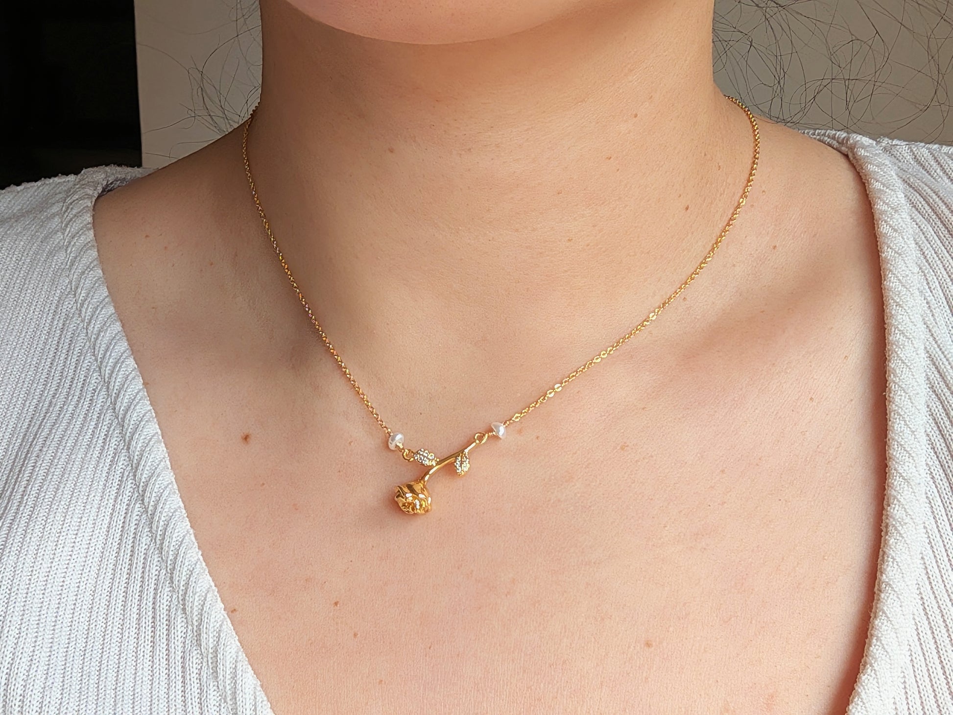 A close-up of a person's neck and chest wearing a delicate gold necklace with a small floral pendant and tiny clear stones.