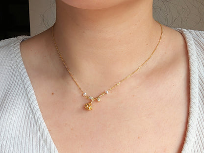 A close-up of a person's neck and chest wearing a delicate gold necklace with a small floral pendant and tiny clear stones.