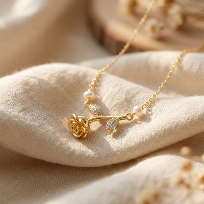 A delicate gold necklace with a rose-shaped pendant, small pearl beads, and clear crystal accents, draped over soft beige fabric.