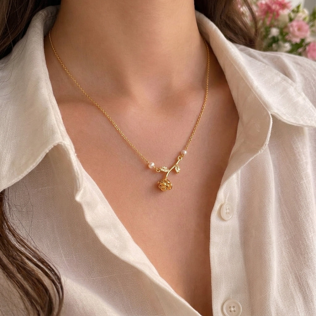 A close-up of a woman wearing a delicate gold necklace with a small floral pendant and pearl-like beads, paired with an off-white linen shirt.