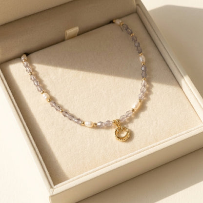 Aesthetic display of the 'Serotonin' dainty smiley face necklace on a stone textured prop, highlighting the purple and gold tones.