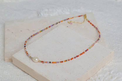 Flatlay display of the Sunrise Whisper colorful beaded necklace with a central freshwater pearl, elegantly resting on a textured stone prop for a minimalist aesthetic by Whisperland Studio.