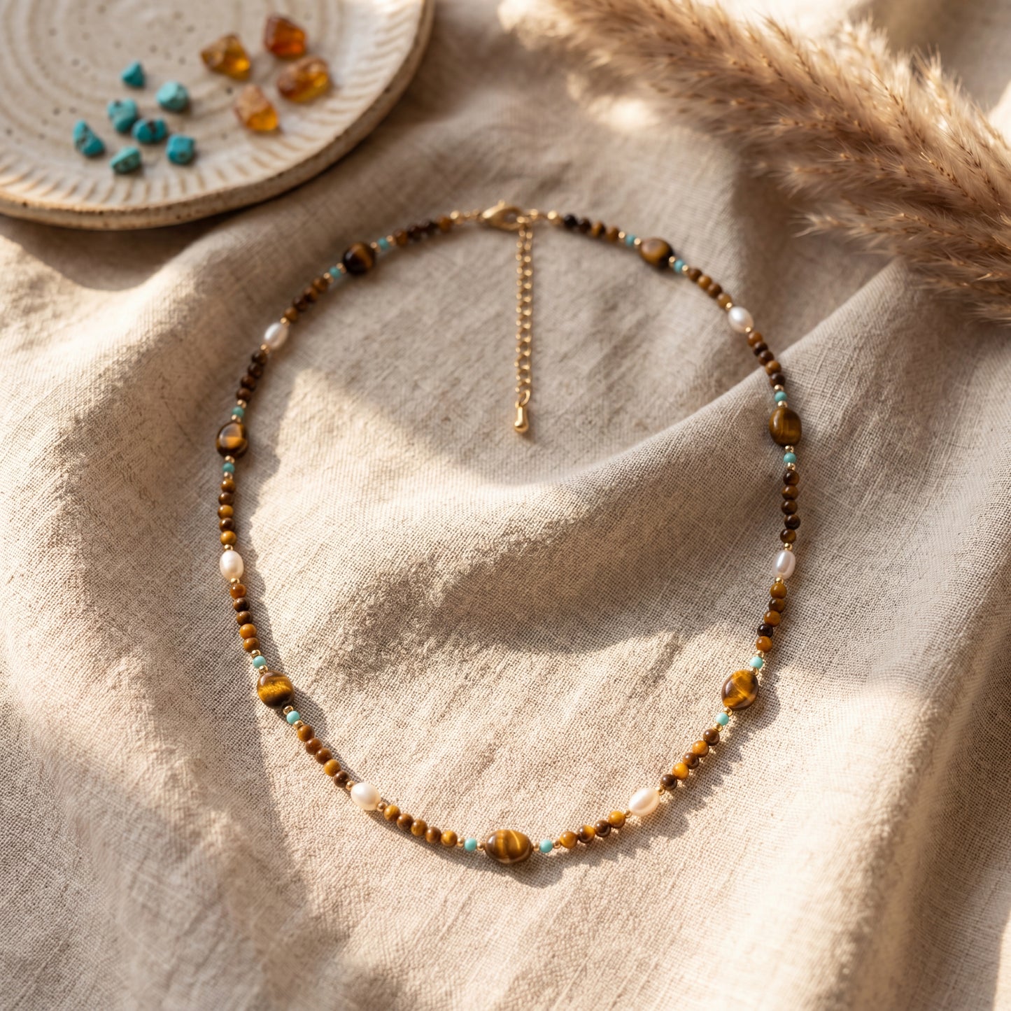 Tierra necklace with natural tiger's eye, turquoise, and natural baroque pearls styled with pampas grass in warm light.