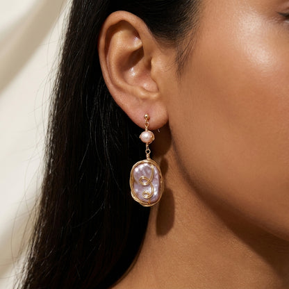 Close-up of a model wearing the Twilight Reverie handmade baroque pearl dangle earrings, showcasing the iridescent purple and gold tones.