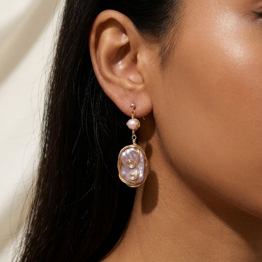 Close-up of a model wearing the Twilight Reverie handmade baroque pearl dangle earrings, showcasing the iridescent purple and gold tones.