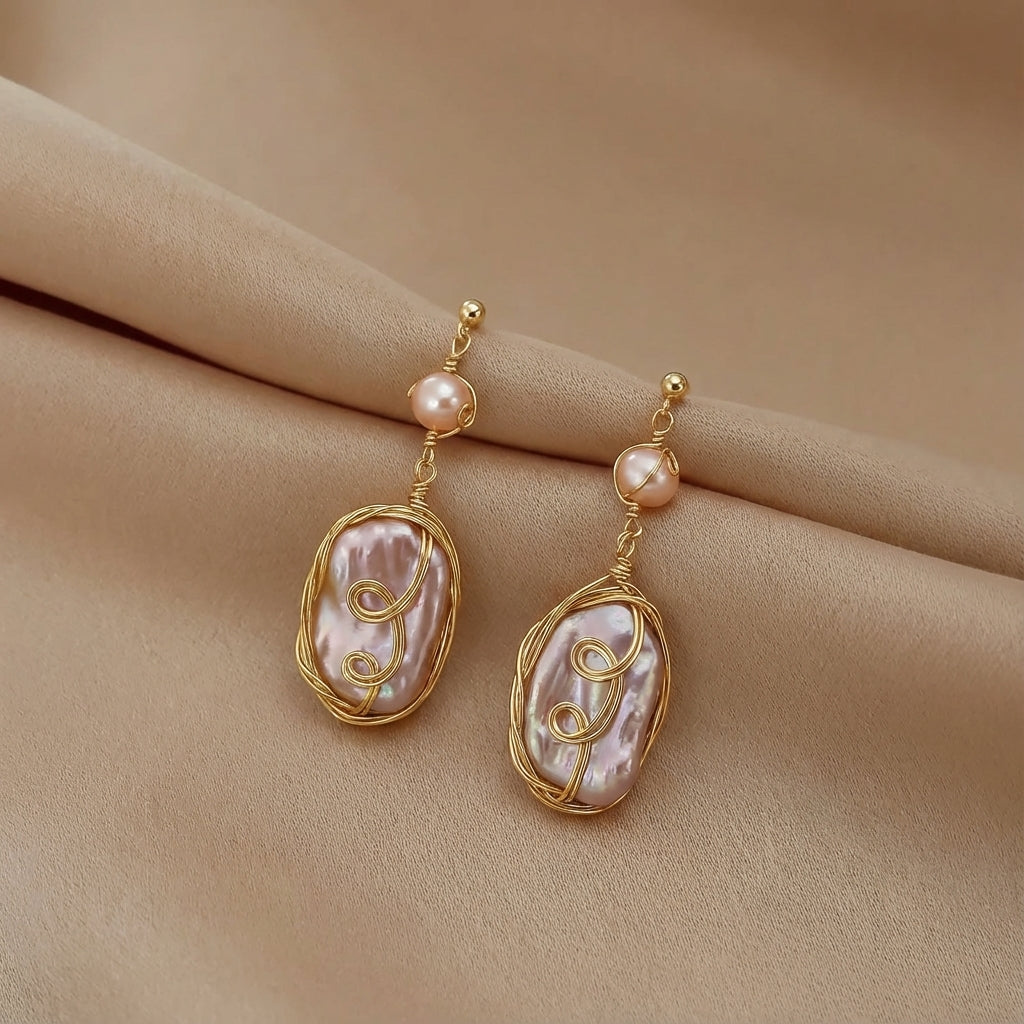 Pair of Twilight Reverie dangle earrings displayed flat, showing the intricate gold swirls and natural oval pearls.