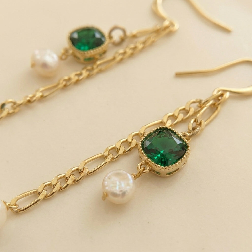 Macro detail of the “Verdant Muse” Emerald and Pearl Drop Earrings showing the square green zircon, dainty pearl, and gold figaro chain